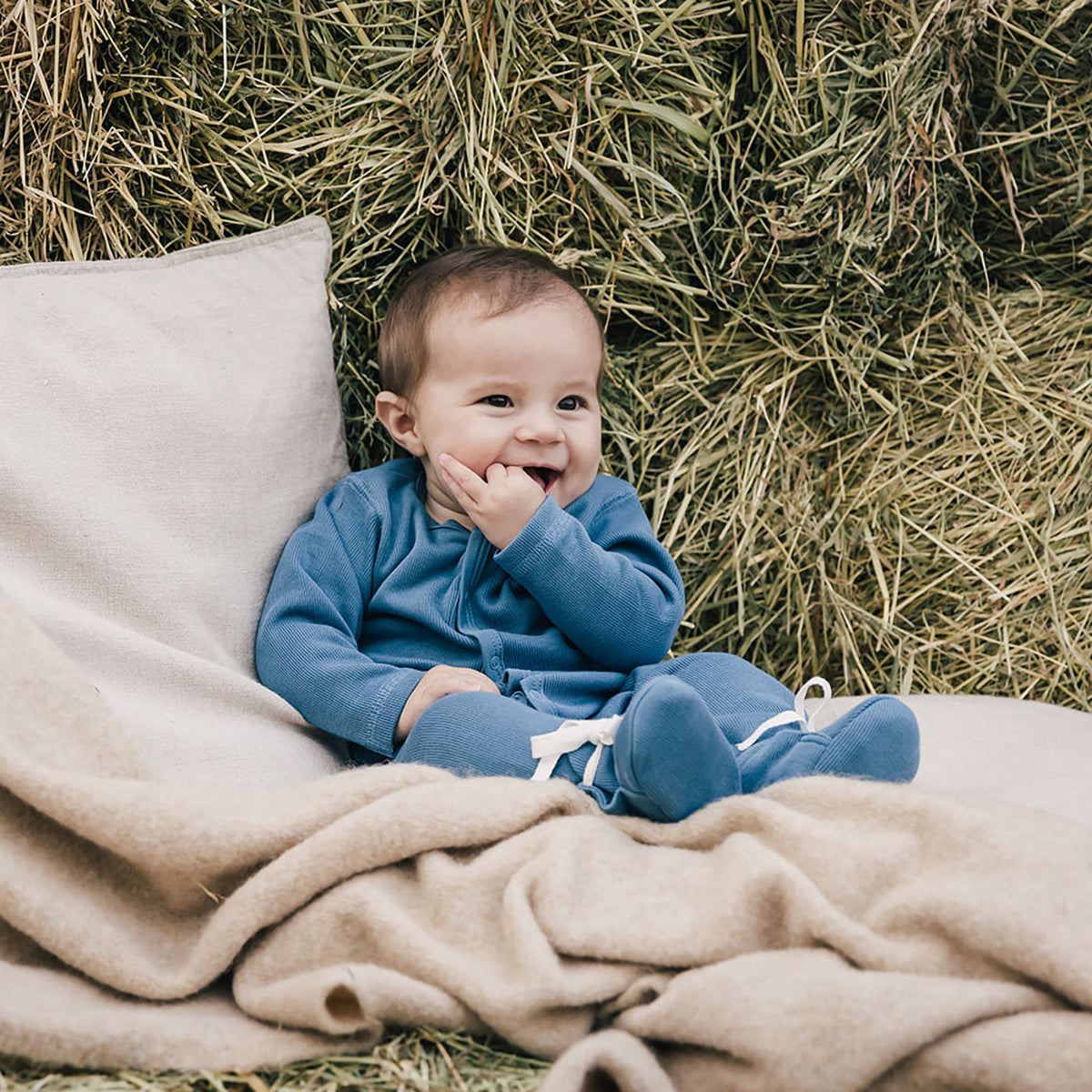 baby on blanket against hay bales wearing uaua romper with baby booties in azul