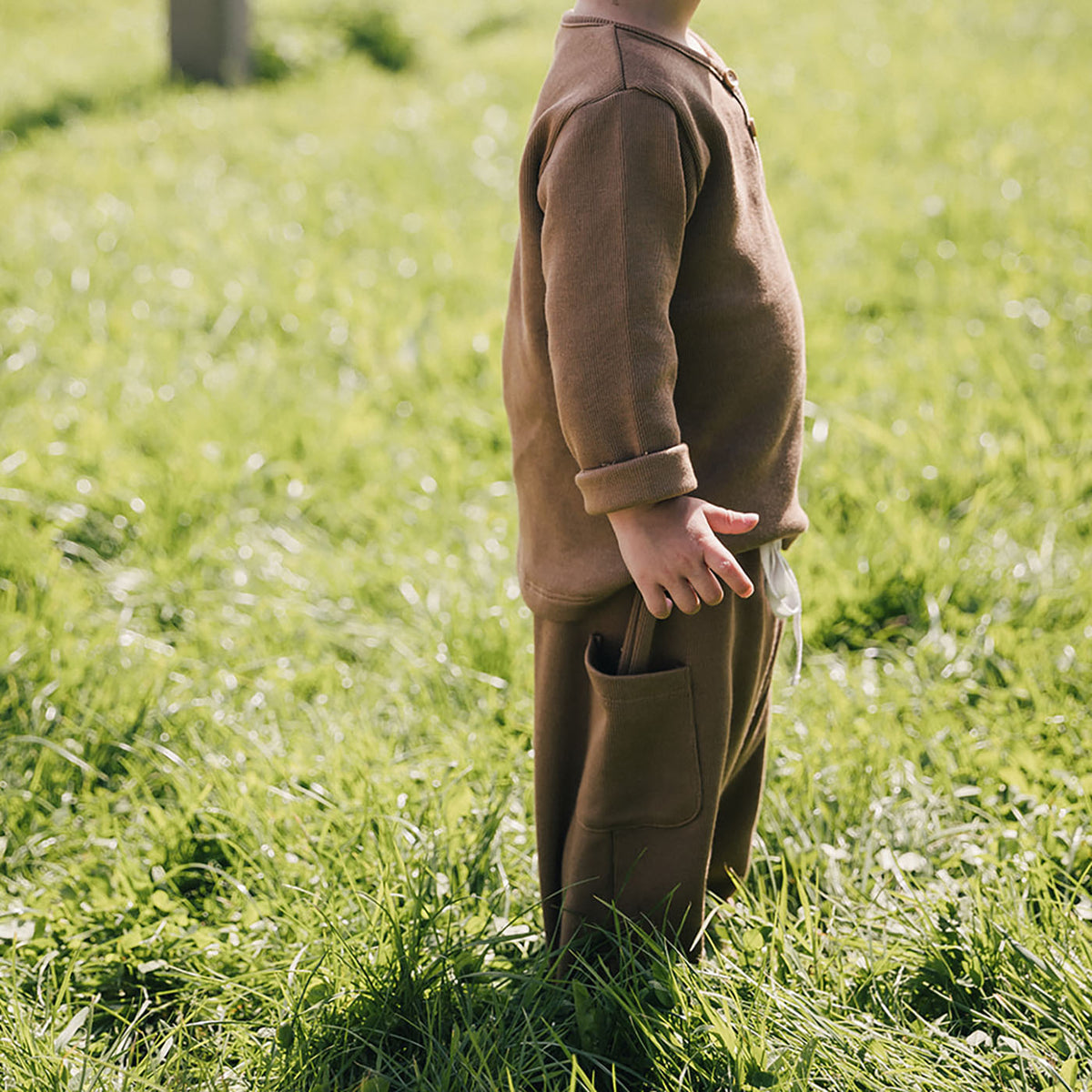 little boy standing sideways in field wearing long sleeve henley in chocolate