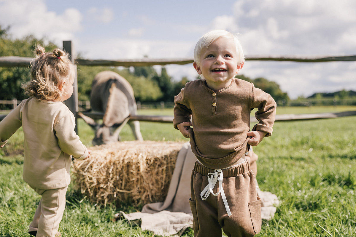 little boy standing, smiling with little girl in field with horse eating hay