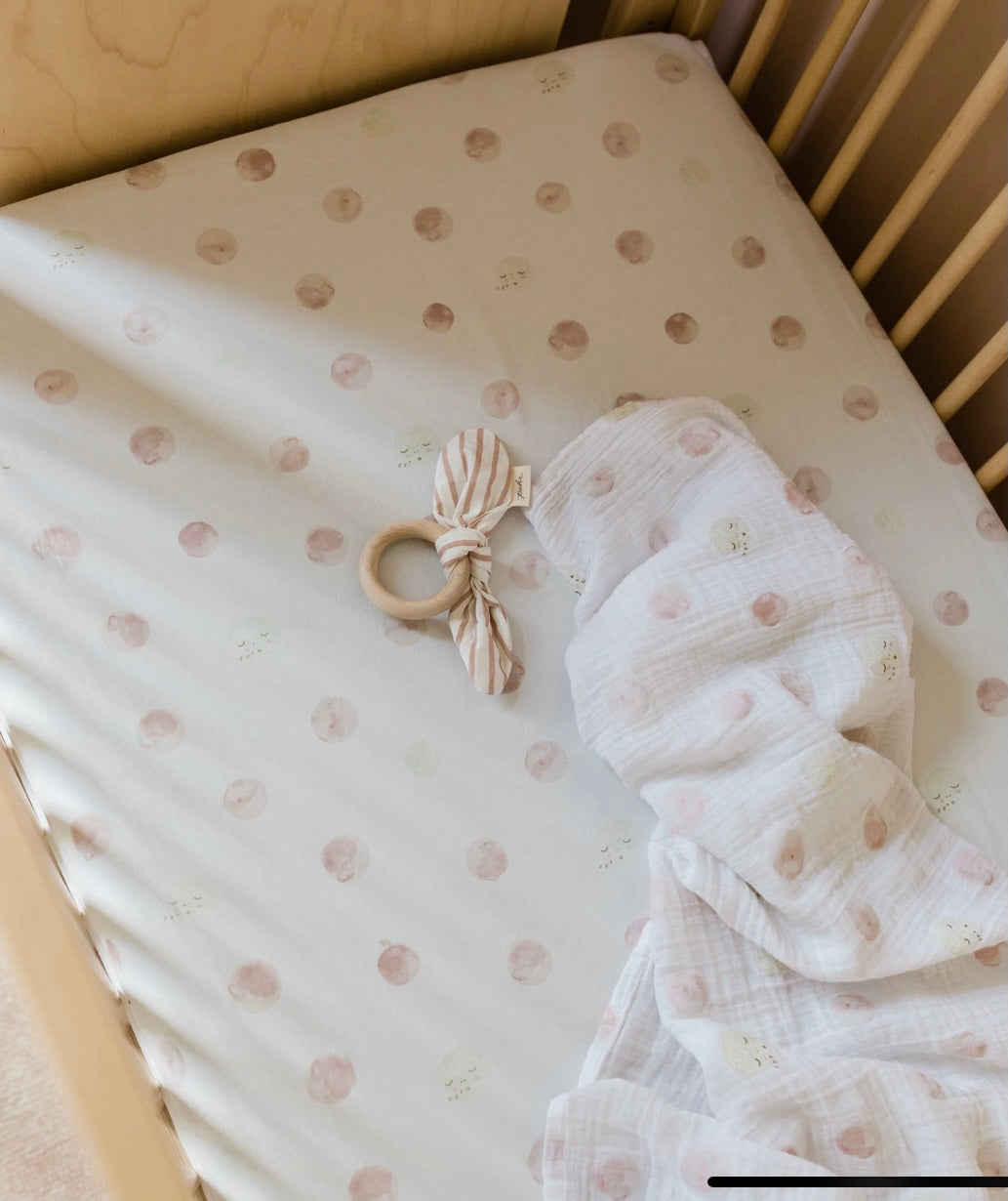 Pehr pink luna dot swaddle in crib with teether