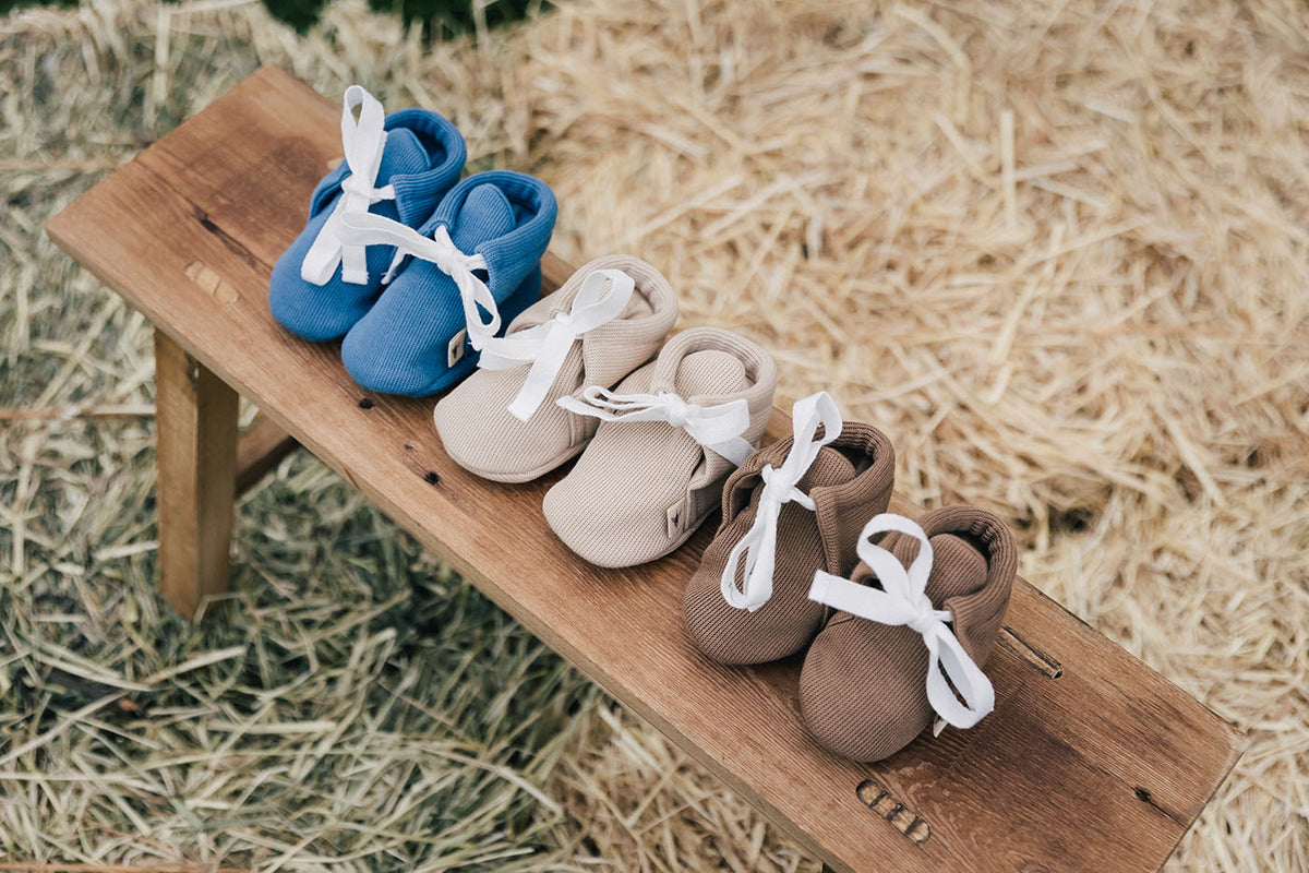 uaua baby booties in chocolate, azul, and biscotti sitting on wooden bench