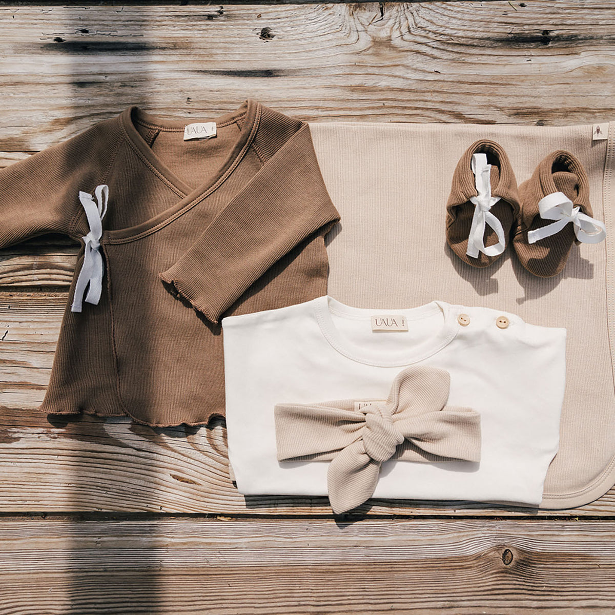 uaua flat lay with baby booties in chocolate, baby bow in biscotti laying on shirt