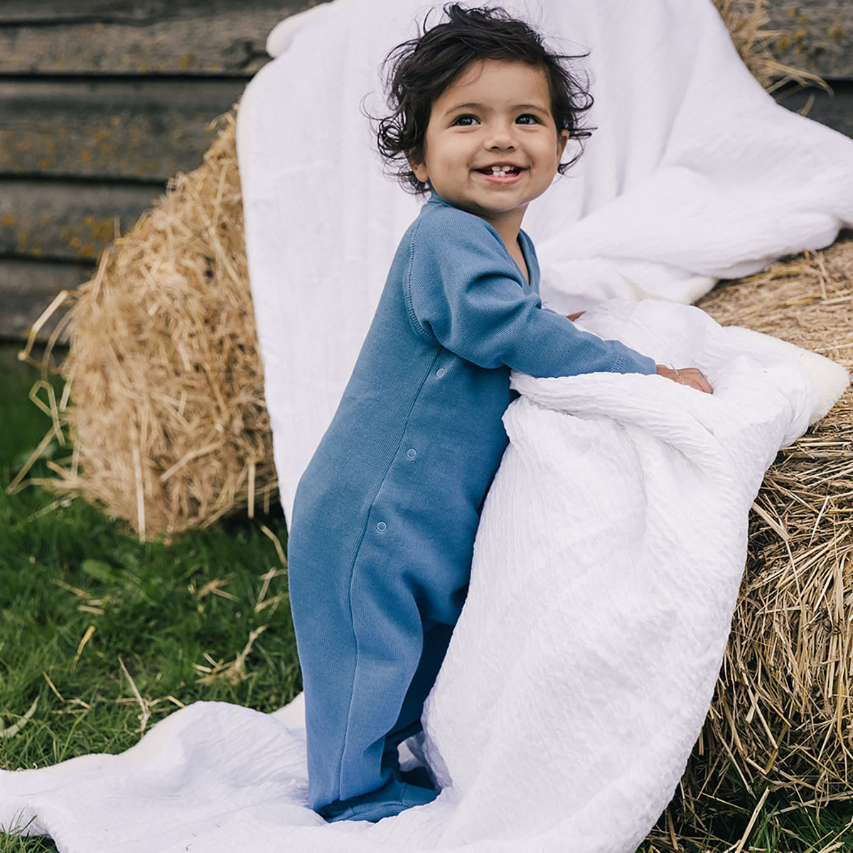 Toddler standing on blanket against hay bales wearing uaua kimono side button footed romper